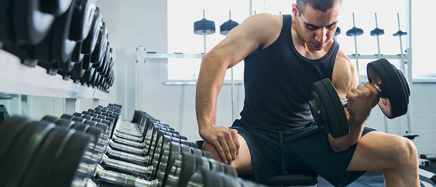 mature man sitting in a gym performing a bicep curl with free weights