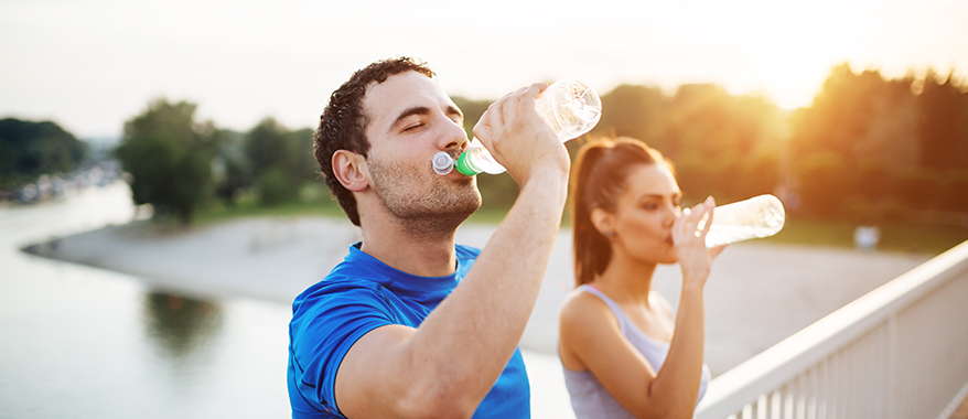 a mature man and woman drinking water on a bridge with water underneath and the sun rising in the distance